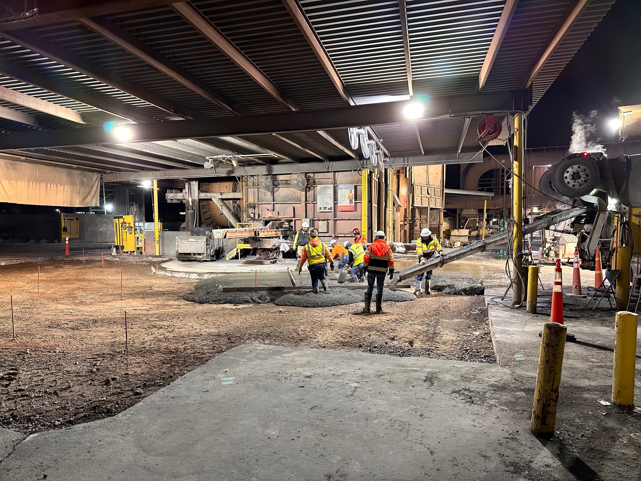 Record crew placing concrete overnight inside an operating plant, working beneath the structural steel