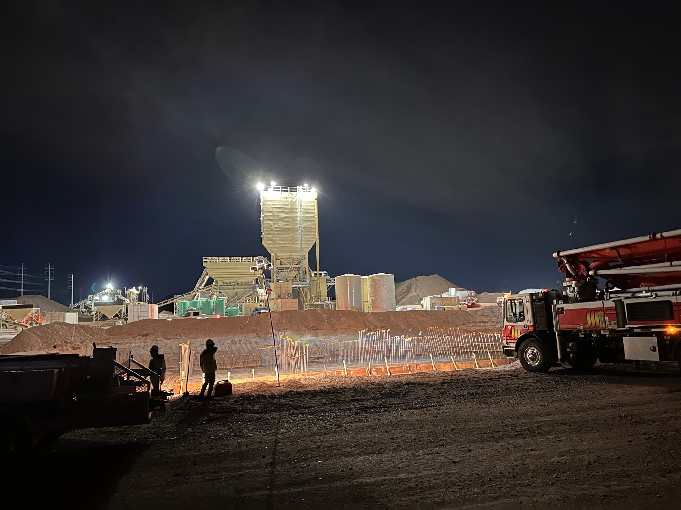 A concrete pump running at night beside a lit plant during a scheduled shutdown